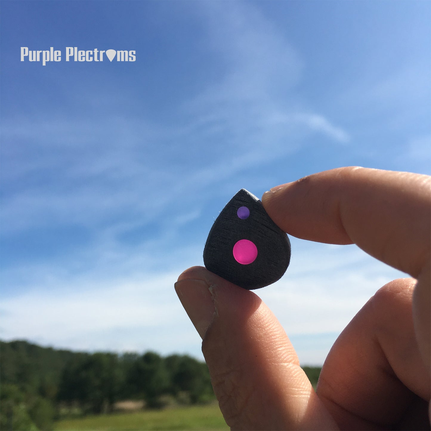 small guitar pick with pink and purple color optics held against a blue sky