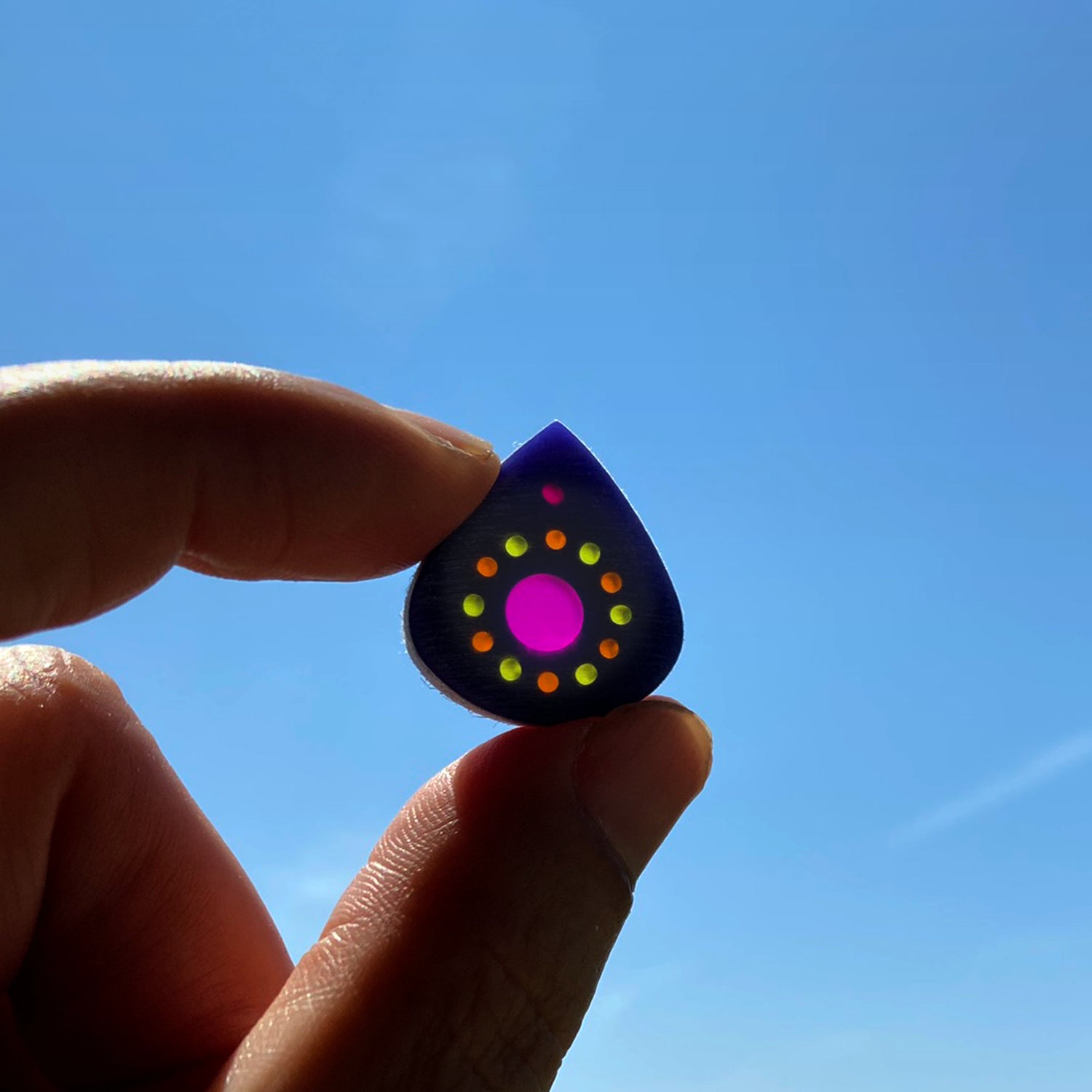 bejeweled small guitar pick held against a blue sky
