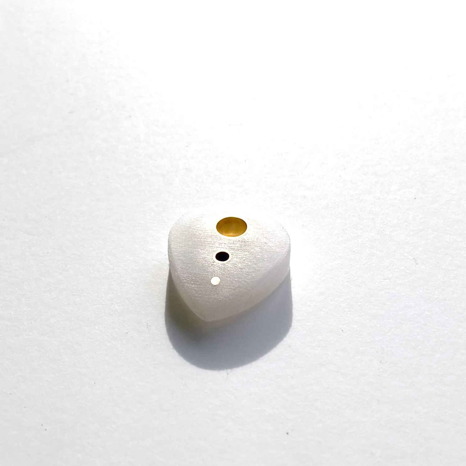 white guitar pick with brass inserts along the spine
