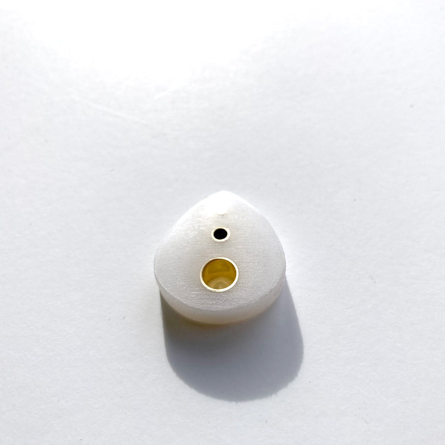white guitar pick with brass inserts along the spine
