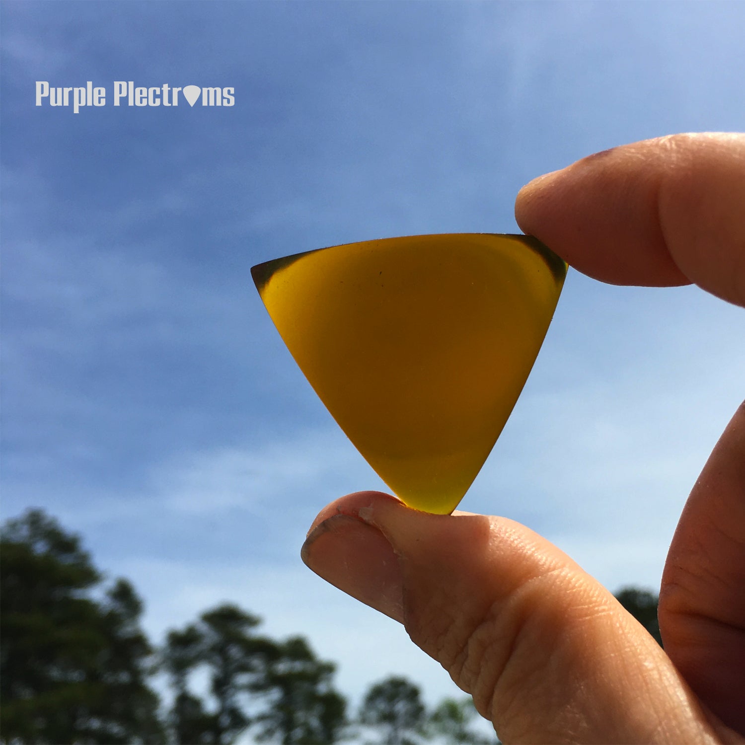 amber color triangular guitar pick held against a blue sky background